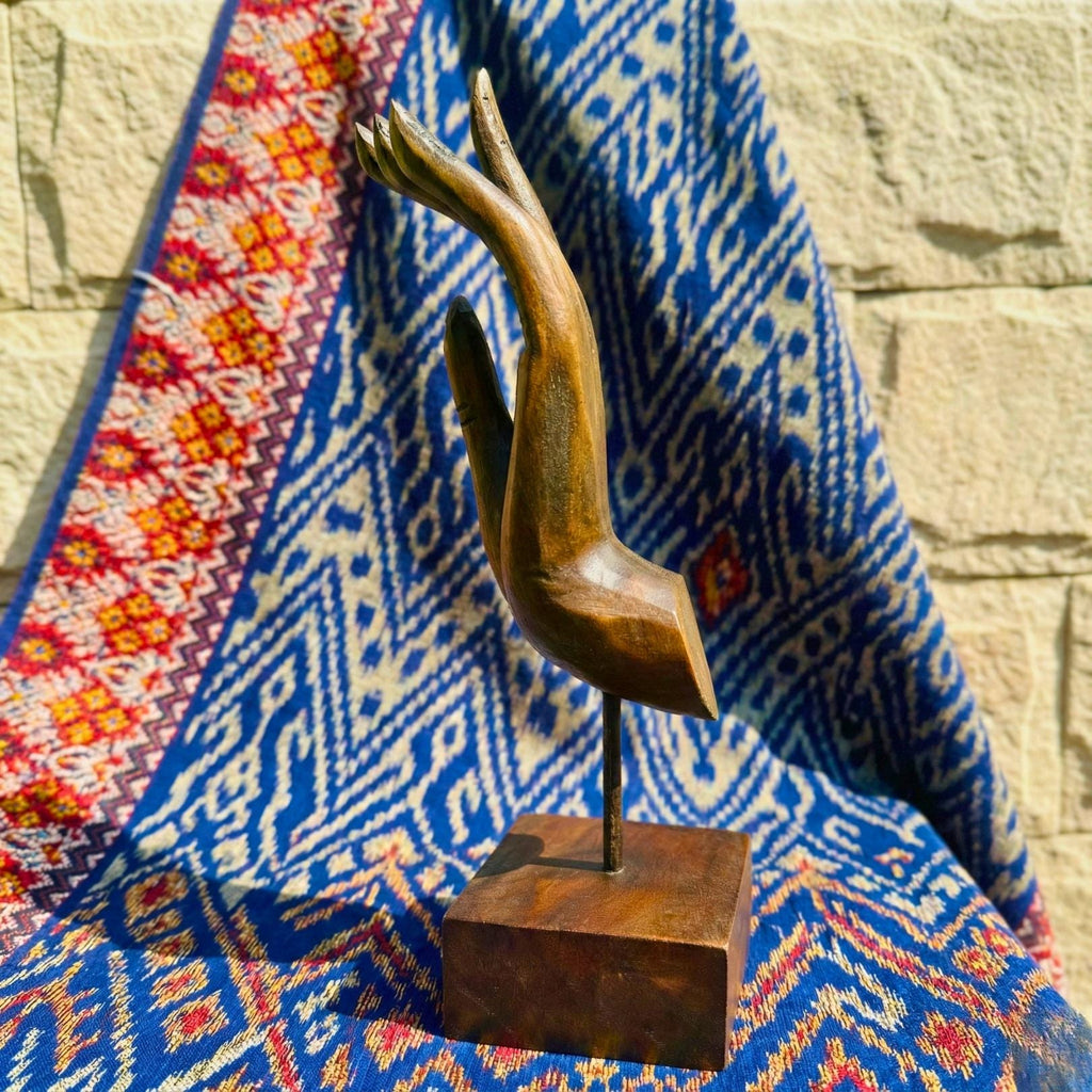 Wooden hand sculpture on a stand with a colorful fabric background