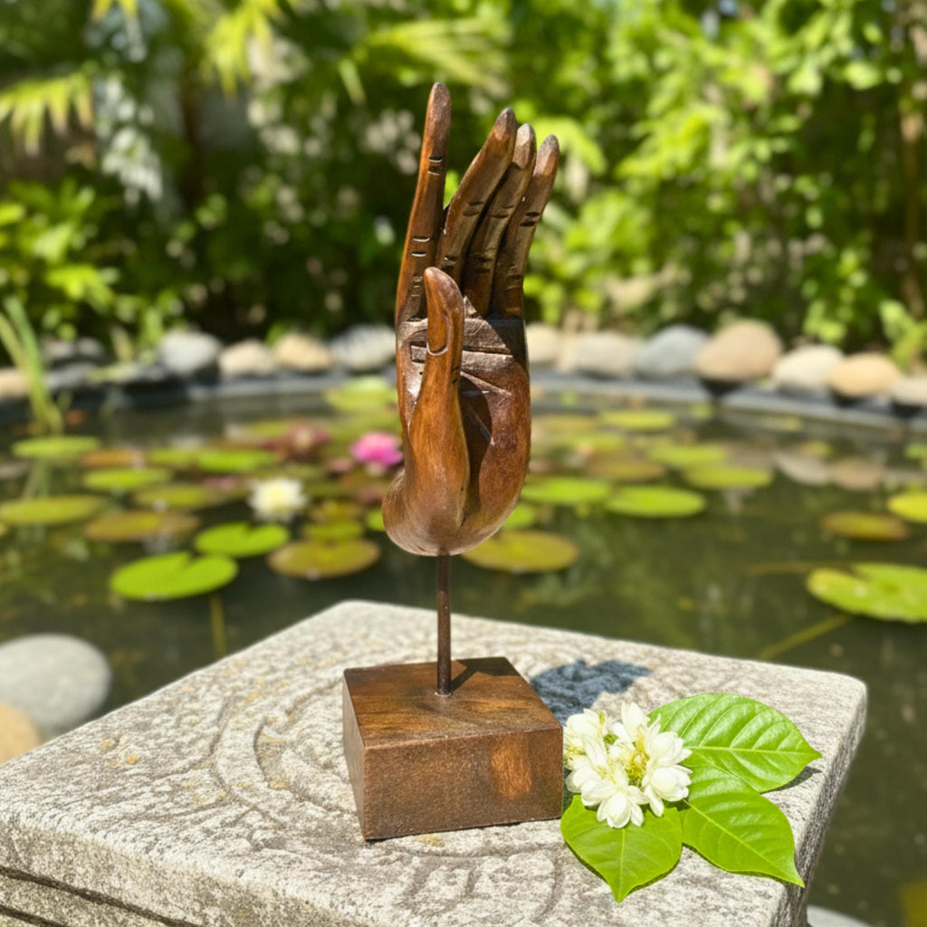 Bronze sculpture of a hand and palm on a stone pedestal with a pond and lily pads in the background.